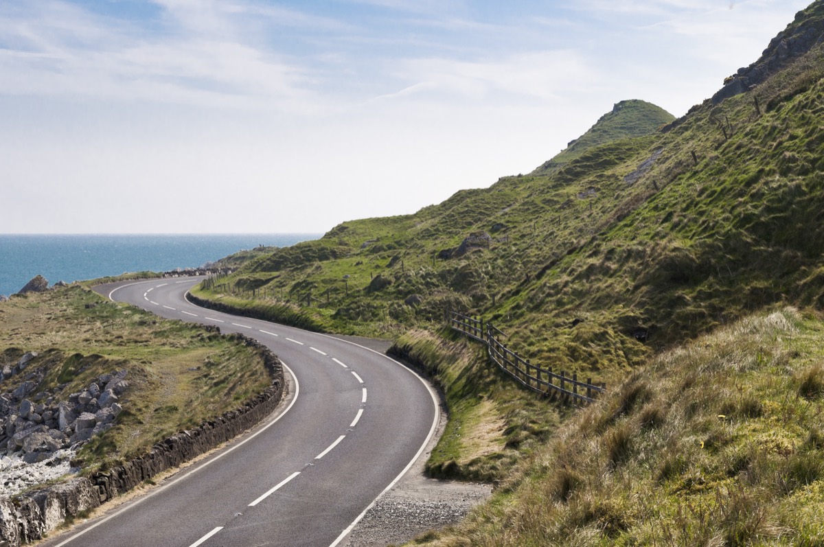 A quiet road winding along green hillsides beside the sea