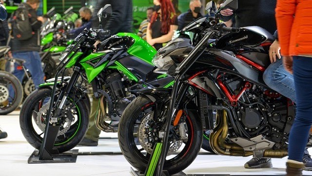 Motorcycles on display stands at a bike show, with visitors walking the floor