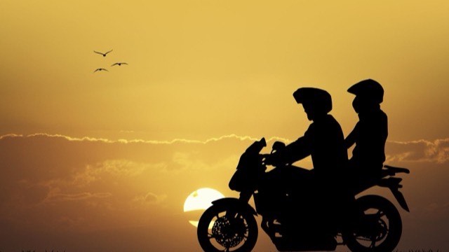 Silhouette of a biker and pillion riding into the sunset