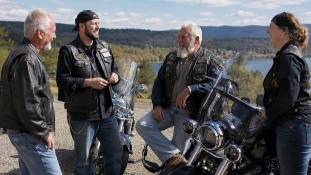 Two riders of different ages smiling together at a café stop, helmets resting on the table