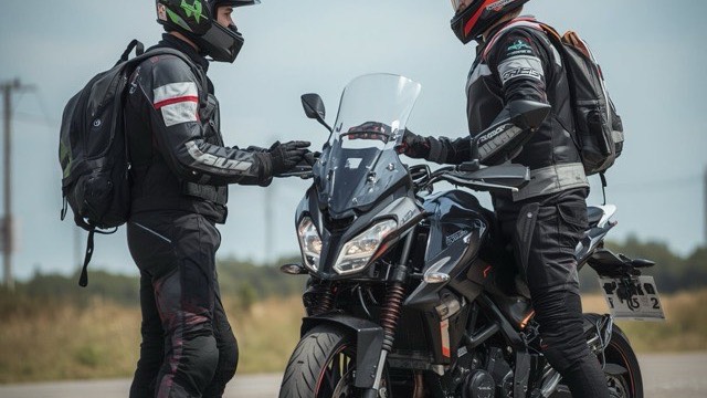 Two riders in full protective gear standing either side of an adventure motorcycle, briefing each other before a ride