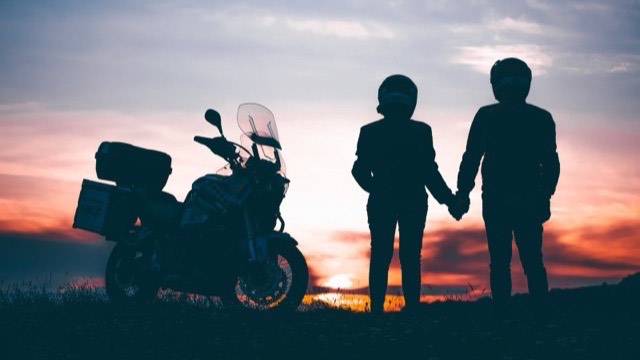 Silhouette of a couple holding hands beside a touring motorcycle at sunset