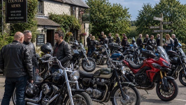 A group of riders socialising in the car park of a traditional British country pub on a sunny day